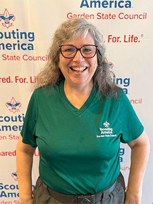 Alyssa G. smiling in a green Scouting America Garden State Council shirt in front of a council backdrop.