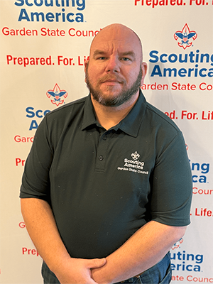 Dan L. standing in a Garden State Council polo shirt in front of a Scouting America backdrop.