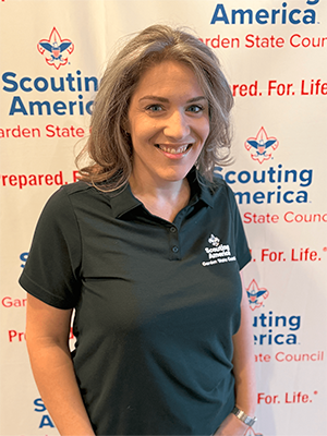 Deanna K. smiling in a Garden State Council polo shirt in front of a Scouting America backdrop.