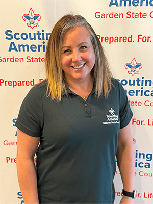 Laurie S. smiling in a Garden State Council polo shirt in front of a Scouting America backdrop.