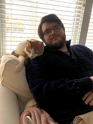 Liam M. seated indoors with an orange-and-white cat resting beside him.