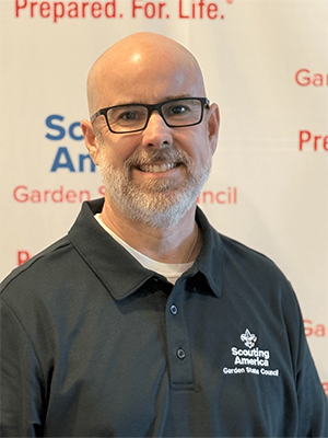 Patrick L. smiling in a Garden State Council polo shirt in front of a Scouting America backdrop.