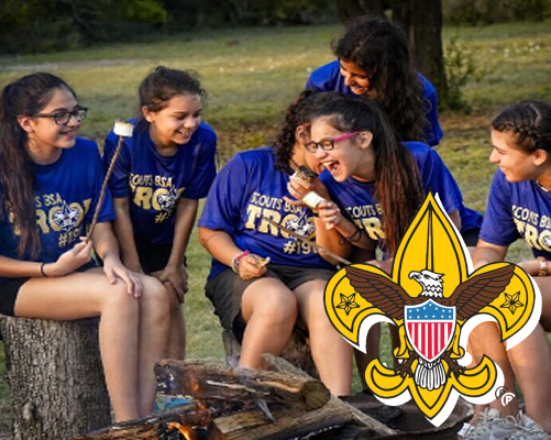 Scouts sitting together around a campfire outdoors with the Scouts BSA logo displayed in the foreground.