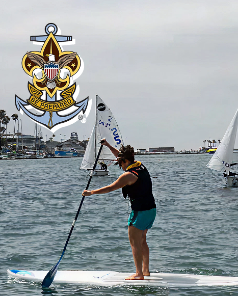 Sea Scout paddleboarding near sailboats with the Sea Scouts emblem displayed above.