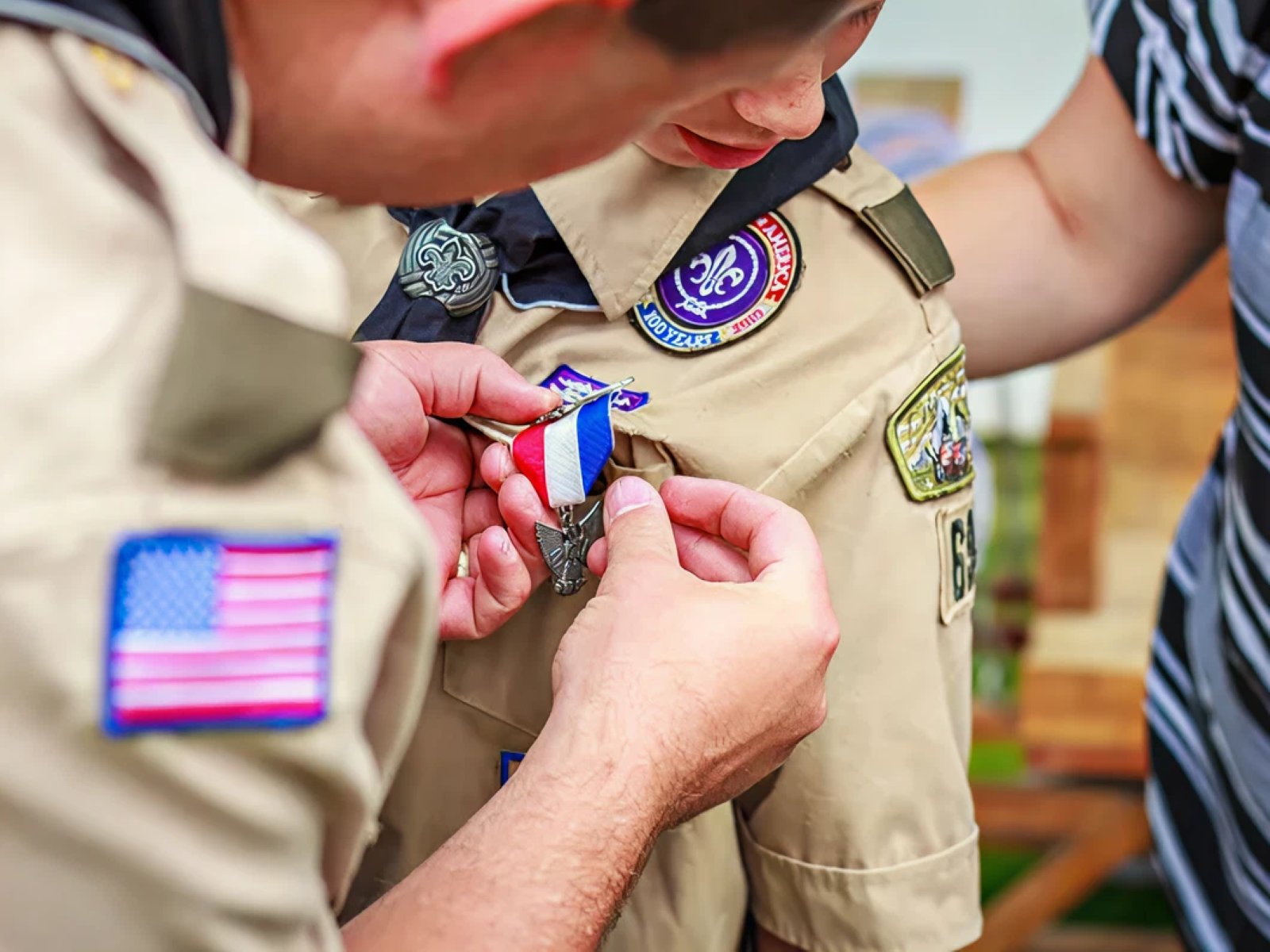 Adult pinning a new badge onto a Scout’s uniform during a recognition ceremony.