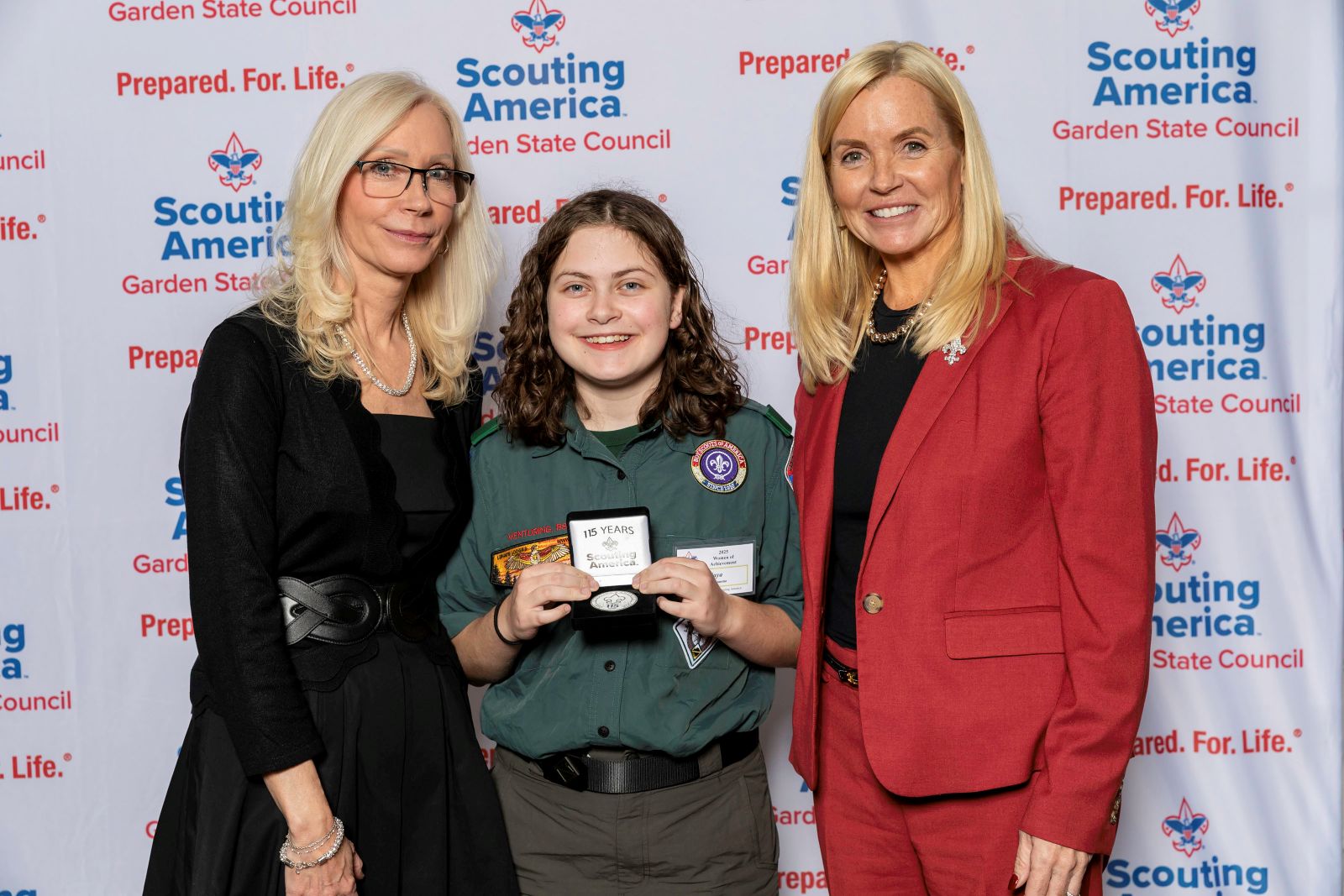 Scout holding a 15-year recognition award while posing with two women in front of a Garden State Council backdrop.