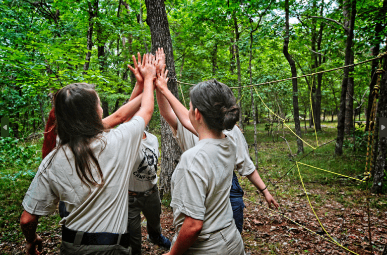 Scouts giving a group high-five during an outdoor team-building activity in a wooded area.