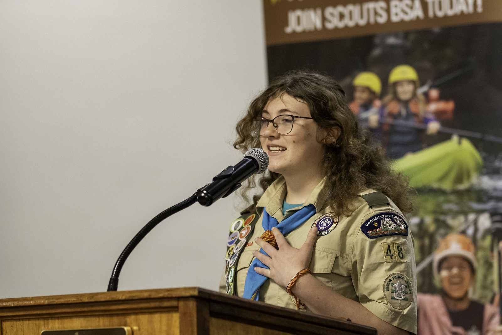 Scout in uniform speaking at a podium with one hand over her heart.