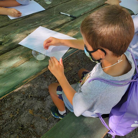 Scout working on a hands-on activity at an outdoor picnic table during summer camp.