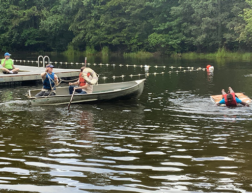 Scouts wearing life jackets practicing canoeing skills on a lake near the camp waterfront.
