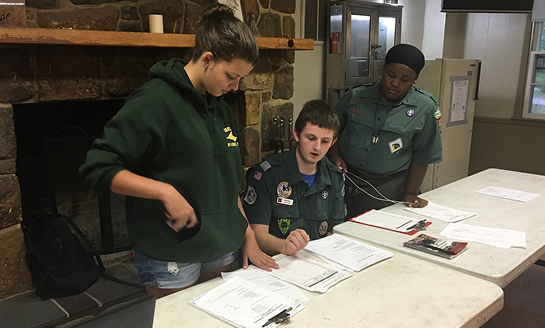Three Scouts reviewing paperwork together at a table during a safeguarding training activity.