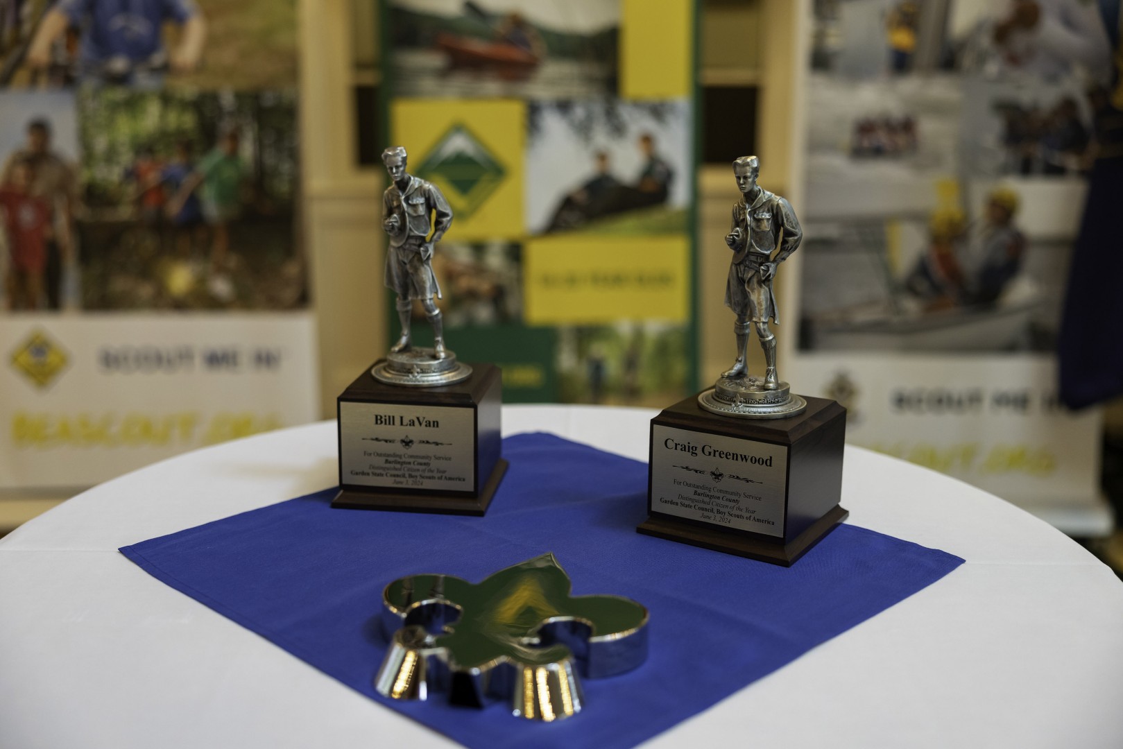 Two Distinguished Citizen Award statuettes displayed on a table in front of Scouting banners.