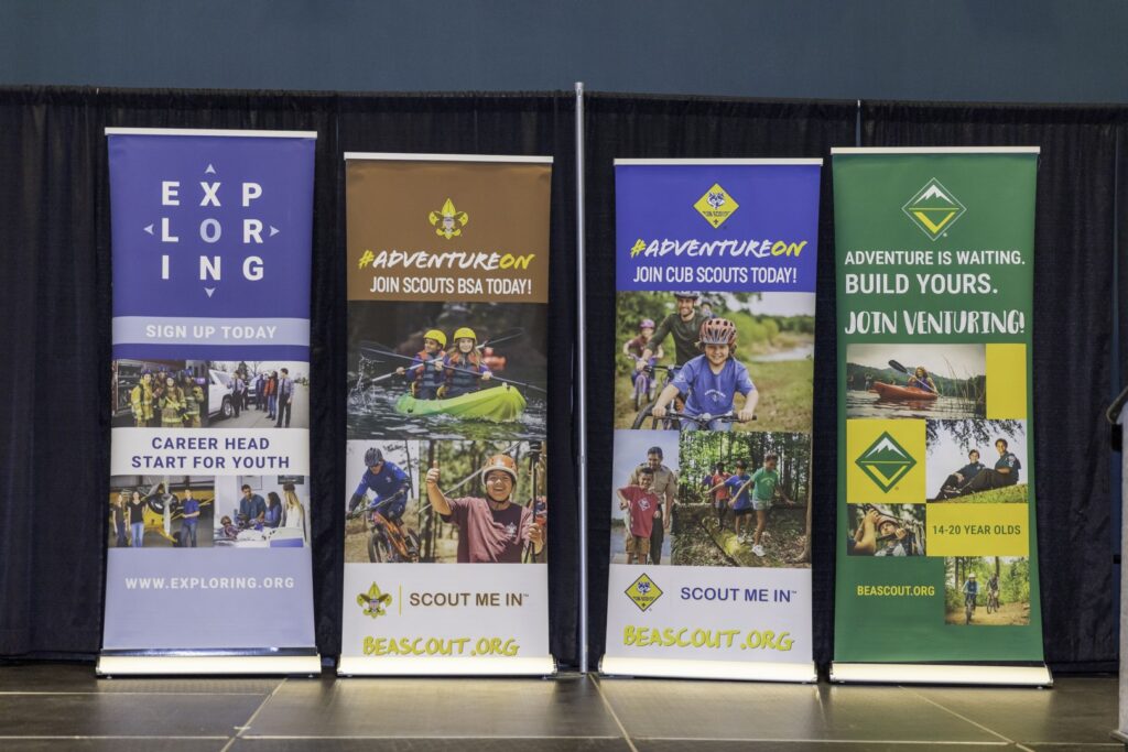 Recruitment banners promoting Exploring, Scouts BSA, Cub Scouts, and Venturing programs displayed at a Scouting event.