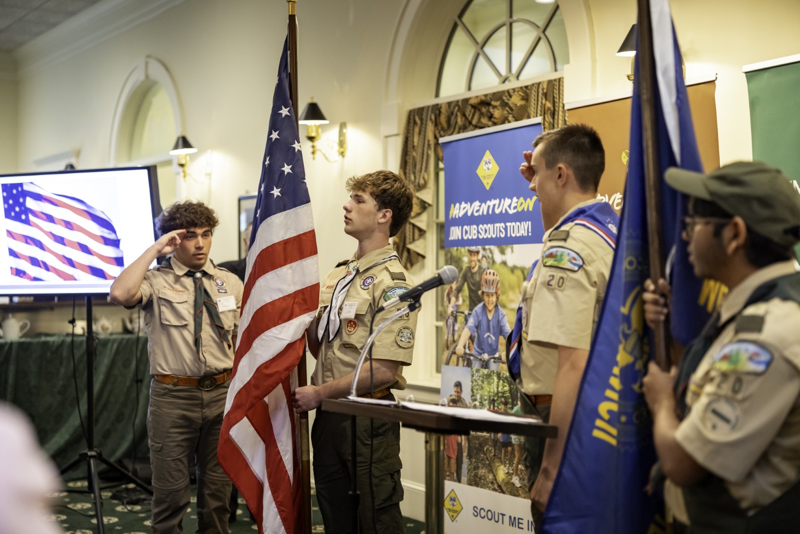 Scouts in uniform presenting the American and council flags during an indoor ceremony.