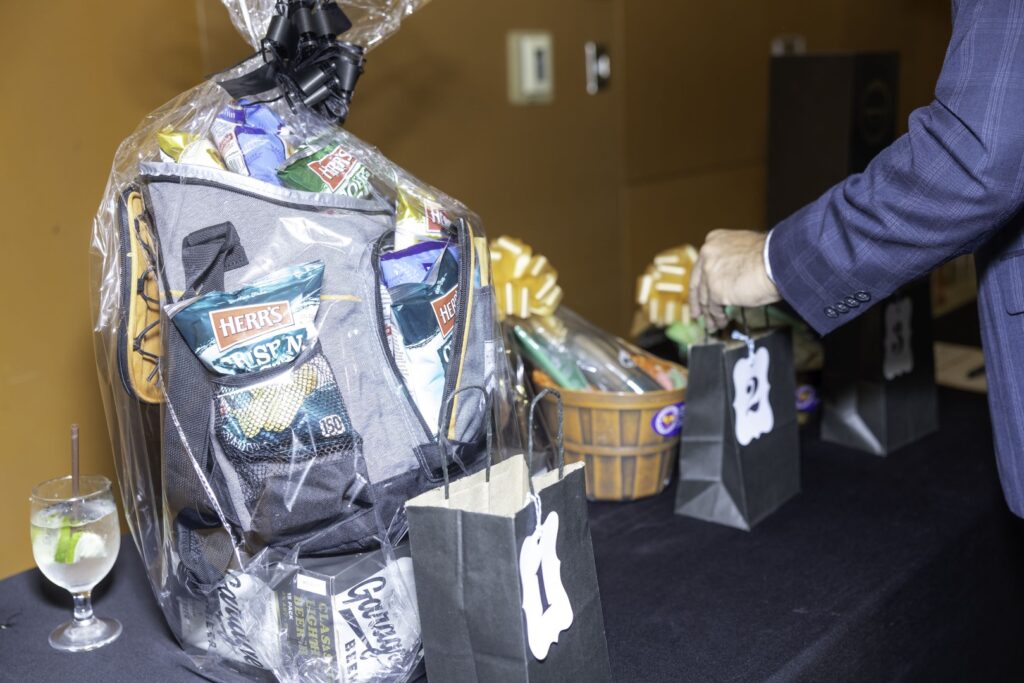 Wrapped gift baskets and numbered bid bags displayed on a table for a silent auction.