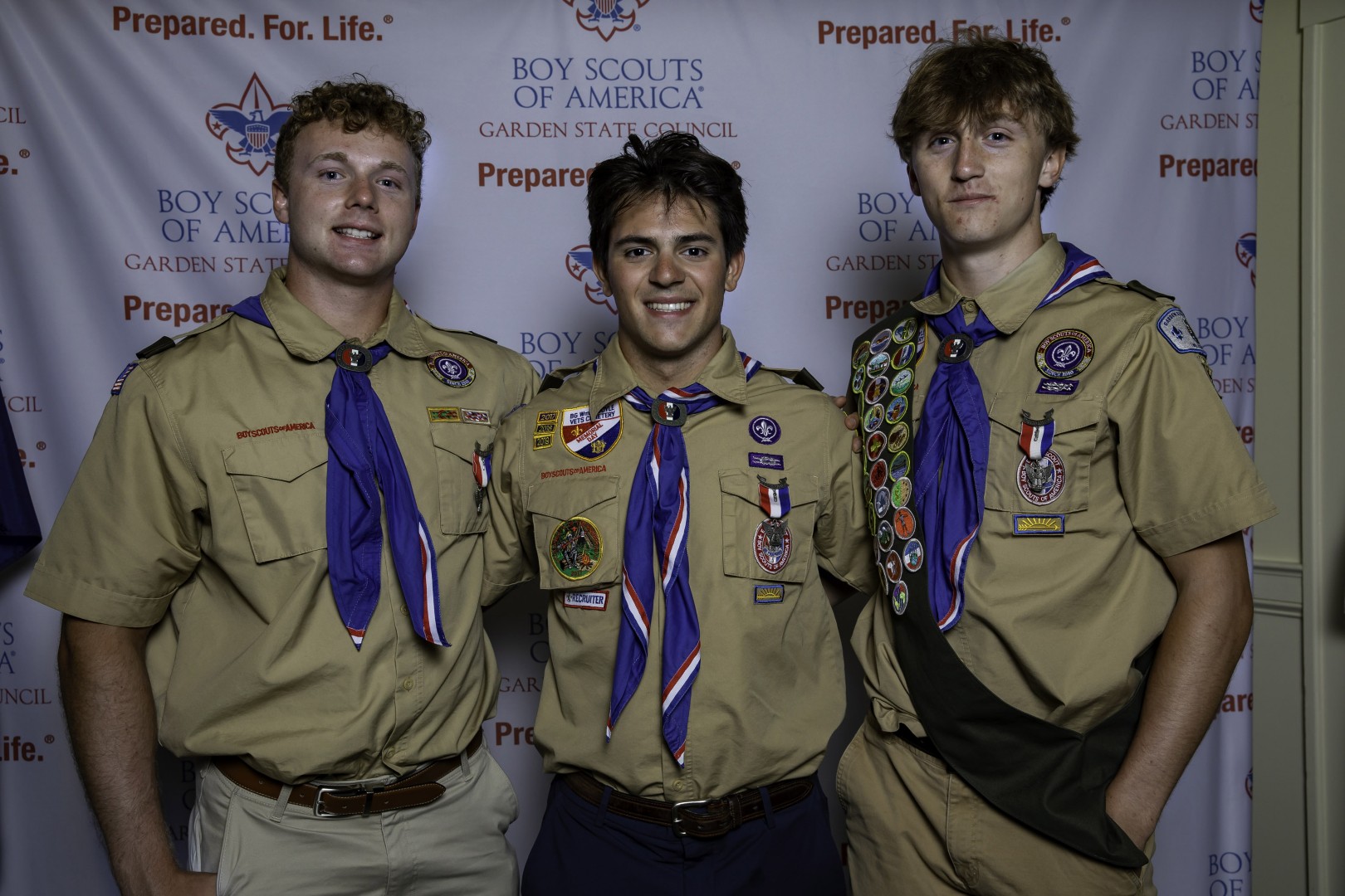 Three Eagle Scouts in uniform posing together in front of a Garden State Council backdrop.
