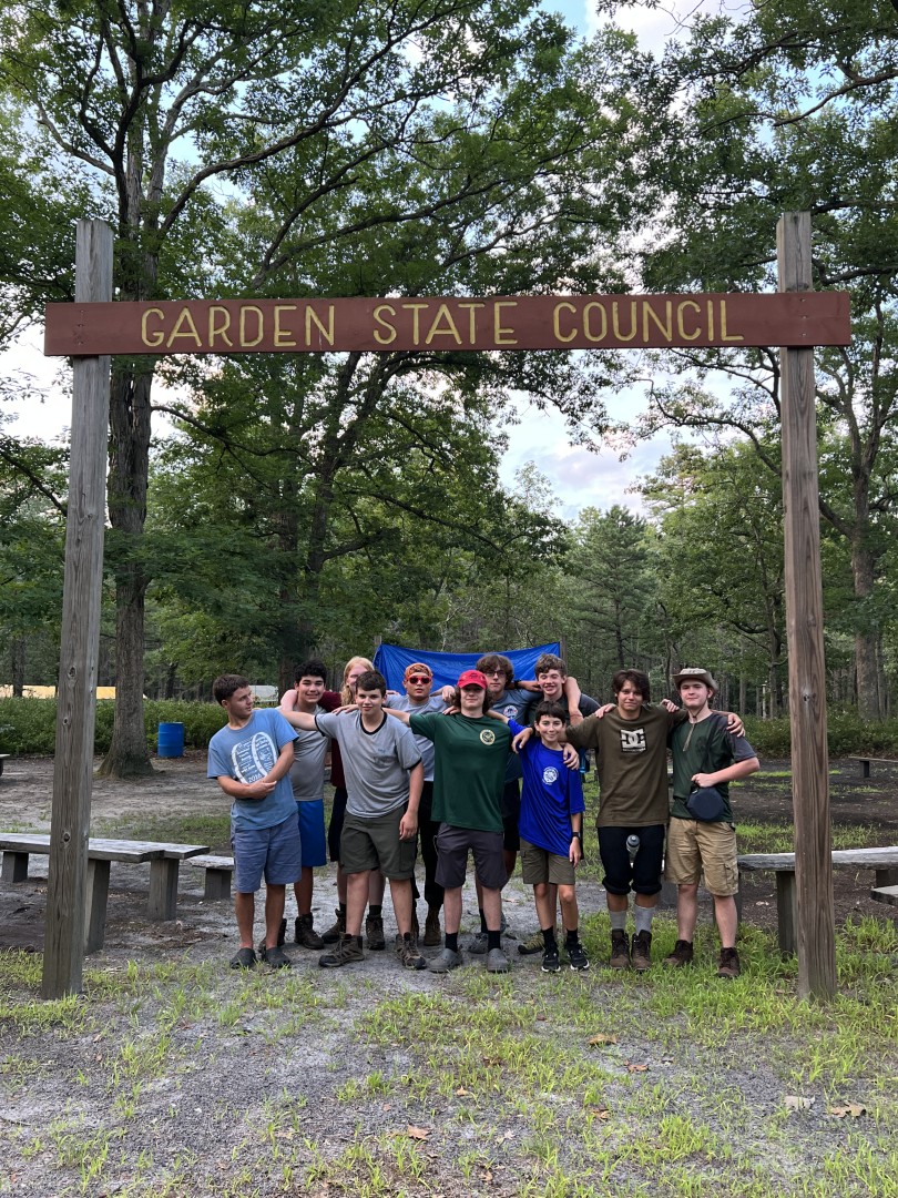 Group of Scouts posing together beneath a Garden State Council sign at 2023 Trek Camp.