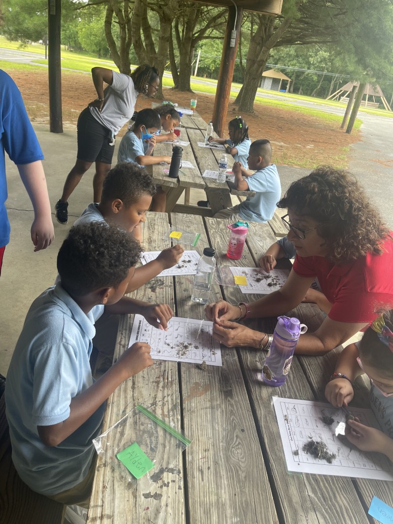 Children working on a hands-on nature activity at picnic tables during 2022 Day Camp in Pine Hill.