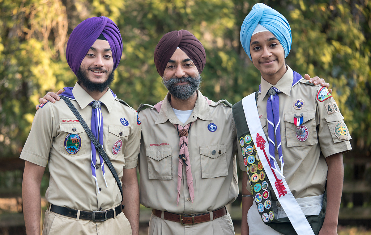 Two Sikh Scouts in uniform posing outdoors with an adult Scouting leader, all wearing turbans.