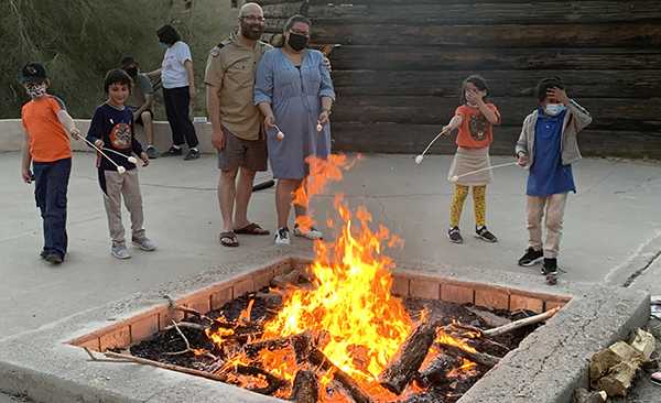 Jewish Scouts and adult leaders roasting marshmallows around a bonfire during a Lag B’Omer celebration.